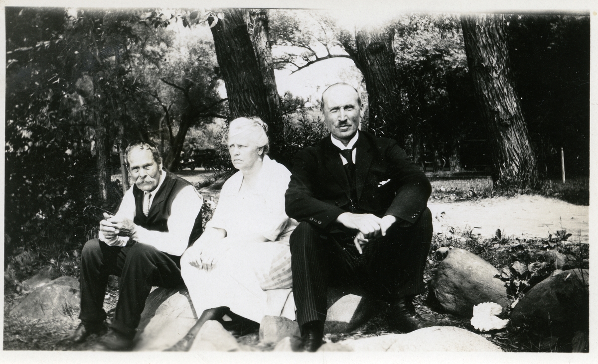 En kvinne og to menn som sitter på en stein i en park. Mannen til høyre er Olaus Islandsmoen.