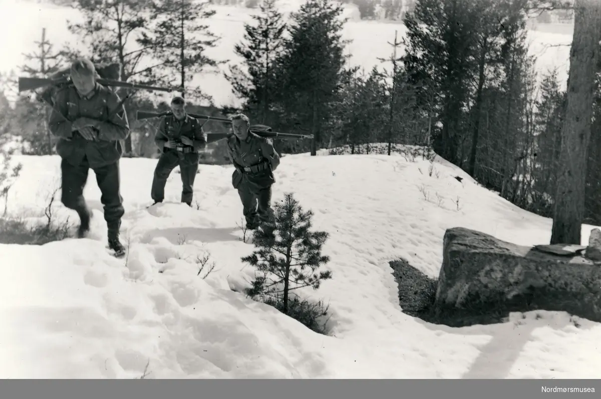 Tre soldater på vei oppover i terrenget med sekker og på toppen av sekken bærer de våpenet sitt.