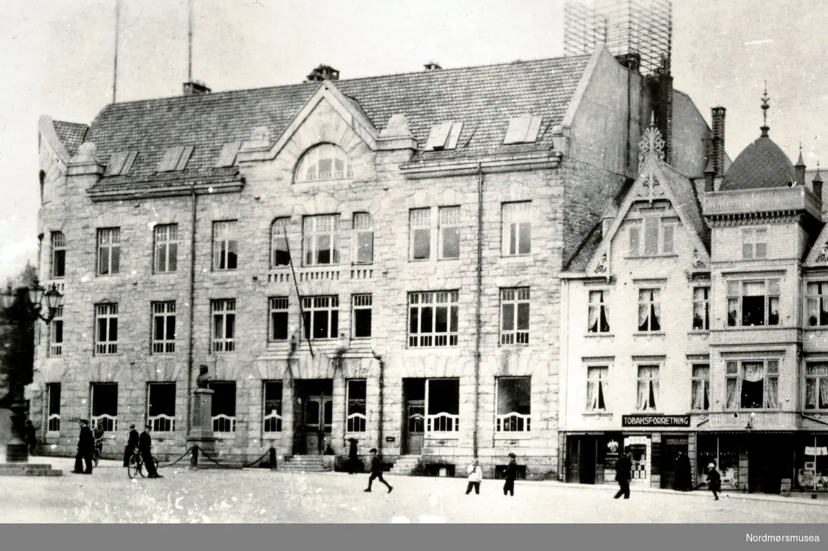 Foto fra Torget på Kirkelandet i Kristiansund, hvor vi ser kommunebygningen som ble bygd omlag 1910 med post og telegraf, deretter følger Glückstadgården. Fra Nordmøre Museums fotosamlinger.