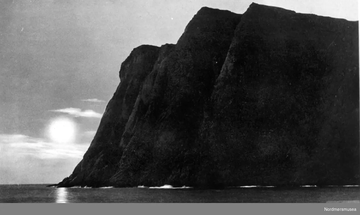 Nordkapp fra sjøsiden, med midnattsolen i bakgrunnen. Postkortet er stemplet ";Eneberettiget Mittet &amp; Co."; fra Nordmøre Museums fotosamlinger.

