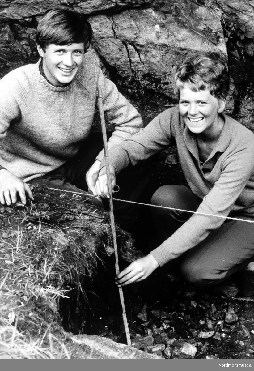 Foto av to arkeologer i arbeid. Trolig omkring 1970, og kan være fra området ved flyplassen på Kvernberget i Kristiansund. serie. Avis/pressebilde fra Romsdalspostens sitt arkiv. Fra Nordmøre Museums fotosamlinger.
