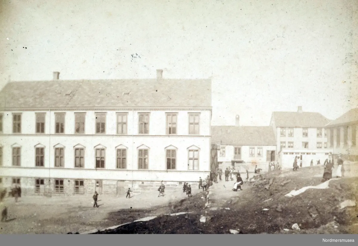 Nordlandet skole, med skoleplana i forgrunnen. Vi ser ellers et par små hus til høyre for skolen. Bildet er datert 1883, og fotograf er Ole Olsen Ranheimsæter. Fra Nordmøre Museums fotosamlinger. 
