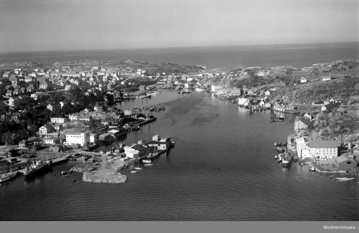Flyfoto fra Vågen i Kristiansund, med Kirkelandet på venstre side og Gomalandet til høyre. Det er Devoldholmen vi ser som ";stikker ut";
 fra Kirkelandet. Datering er ukjent, men er trolig fra omkring 1950 til 1960. Fra Nordmøre museums fotosamlinger. Reg: EFR
