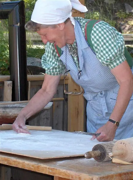 Dame står ute og baker flatbrød. Her fordeler hun mel utover bakstbordet.