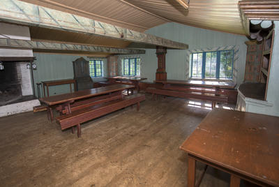 Barfrøstua har tregolv, grønnmalte laftede tømmervegger, stor peis og møblering med langbord og benker.