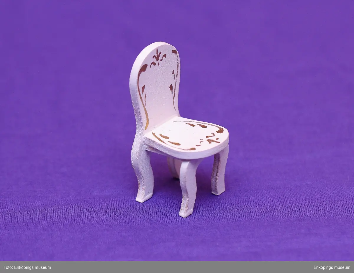 Vitmålad stol med gulddekor på säte och rygg.