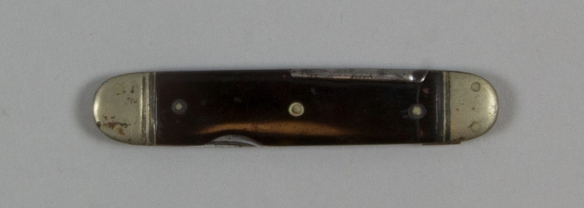 Kniv, pennkniv, av stål och möjligen bakelit. Två uppfällbara smala knivblad och troligen piprensare. Ett blad avslaget.