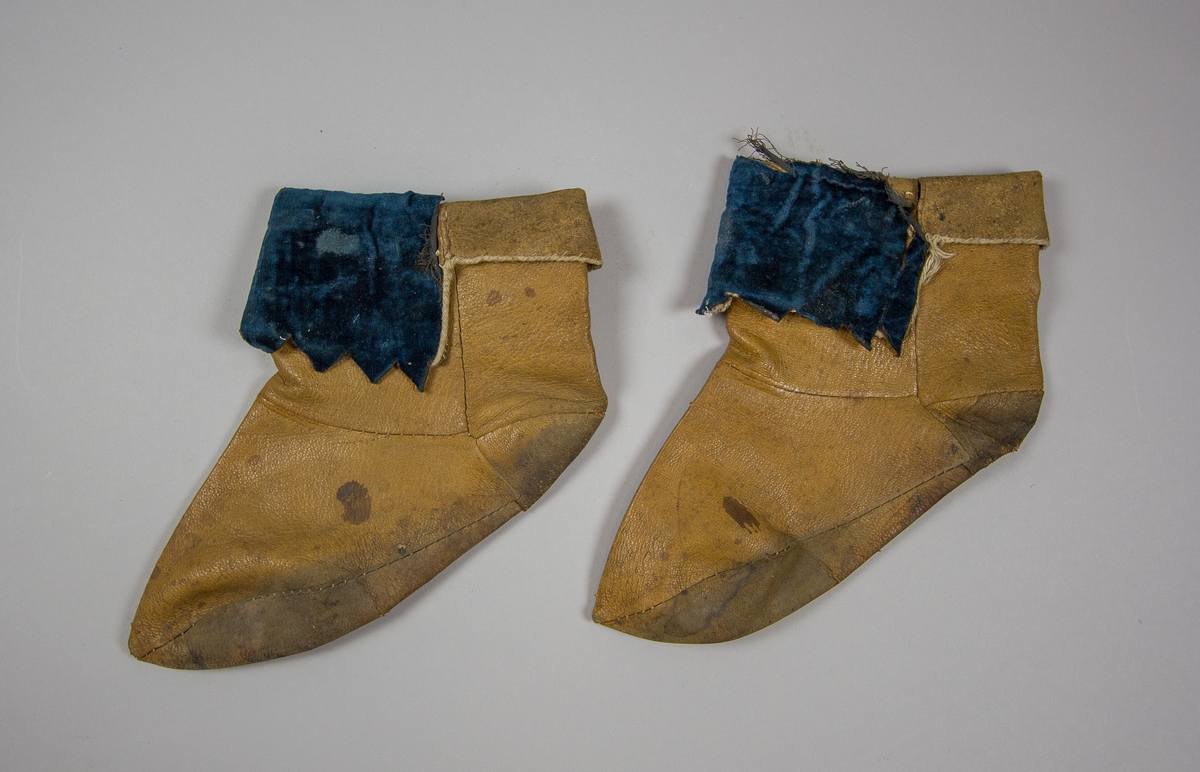 Skor, 1 par, av brunt läder som går upp över vristen, sammanfogade av flera delar. Påsydd dekoration av blå sammet på den nedvikta kanten.