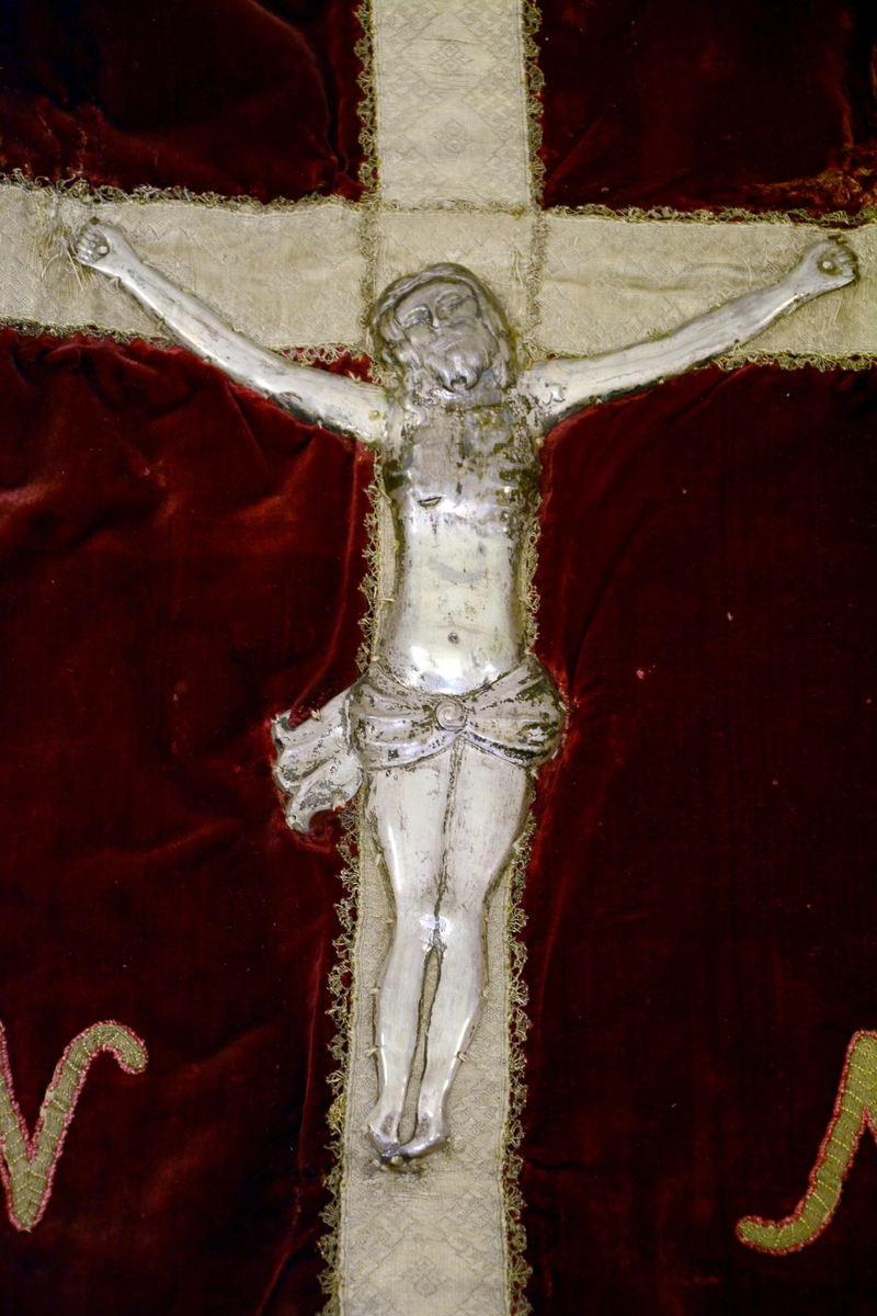 Kristus figur med armene opp i sølvrelieff. Montert på kors av silkebånd.