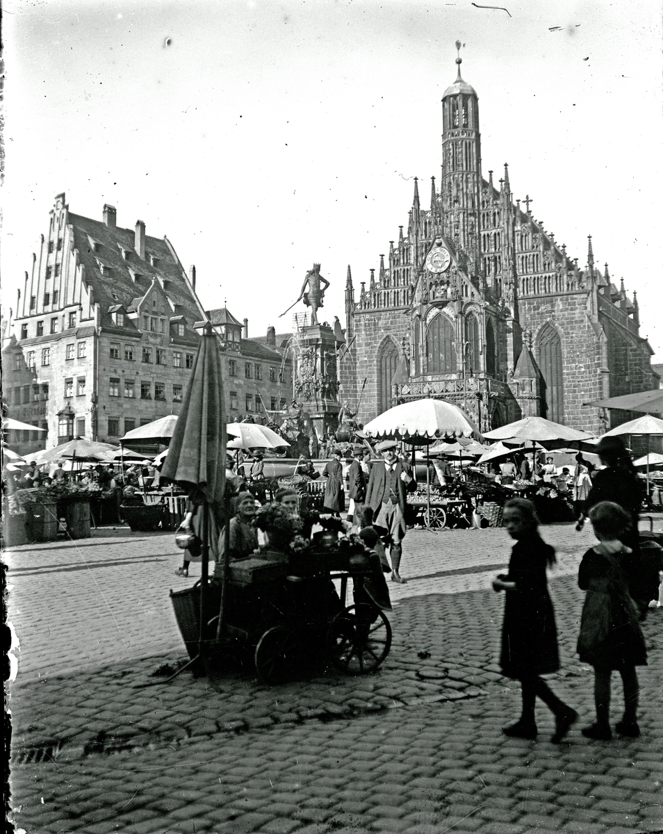 Fotografi av Hauptmarkt, med Frauenkirche i bakgrunden, tillsammans med Neptunbrunnen, i Nürnberg. Taget på tidigt 1900-tal. Fotograf möjligen Alfred Bergendahl.