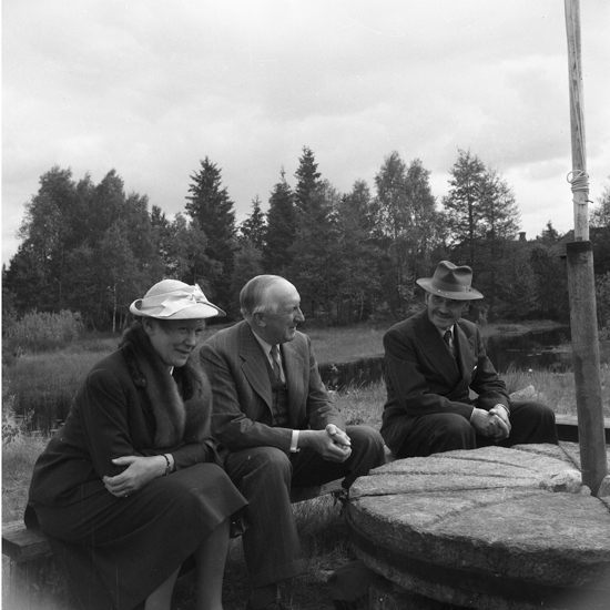 Två män och en kvinna som sitter på en bänk vid ett runt bord.