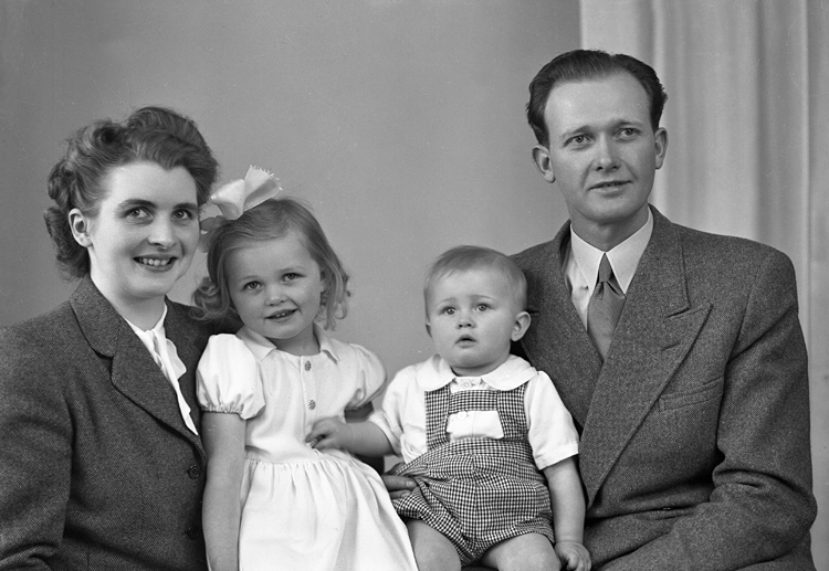 Foto av en familj med två små barn (en flicka och en pojke).
Midjebild. Ateljéfoto.
Trol. : Simon Göte Andersson (1915-1998), Virestad. Gift 1945 med Greta Mebel Ingeborg (1924-1998).
Källa: Sveriges Dödbok 1901-2009.