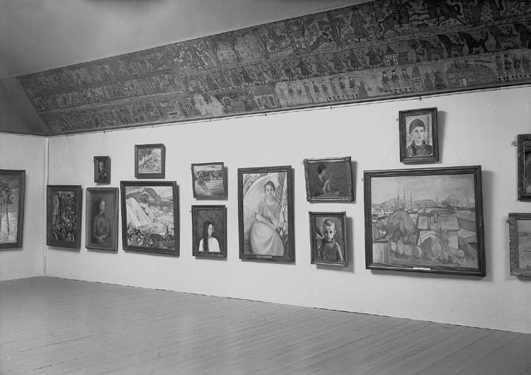 En tavelutställning i Smålands museum, i dåv. textilkammaren.
Till höger på väggen hänger ett antal tavlor och en avlång målad bonad.