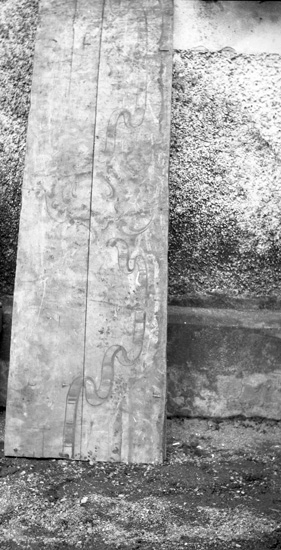 Foto på en bräda som står lutad mot kyrkväggen.