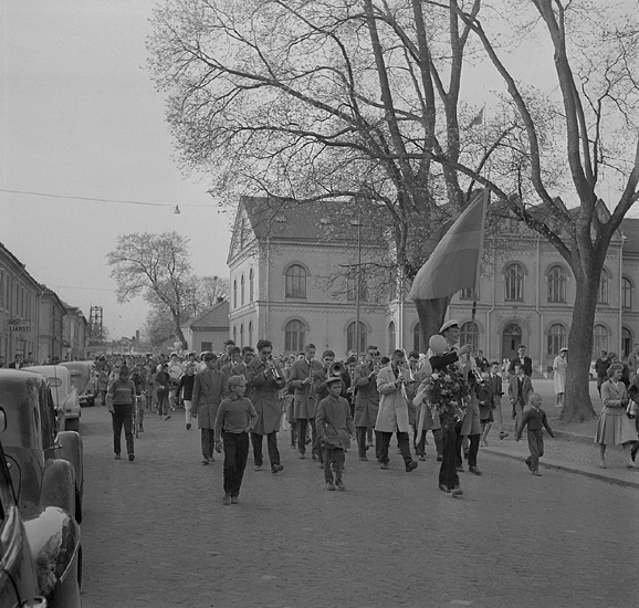 Studenterna fjärde dagen, 1959. 
Studenterna m.fl. tågar utmed Skolgatan, på väg mot Linnéparken och talet vid Esaias Tegnérs staty. 
I bakgrunden syns Norrtullskolan.