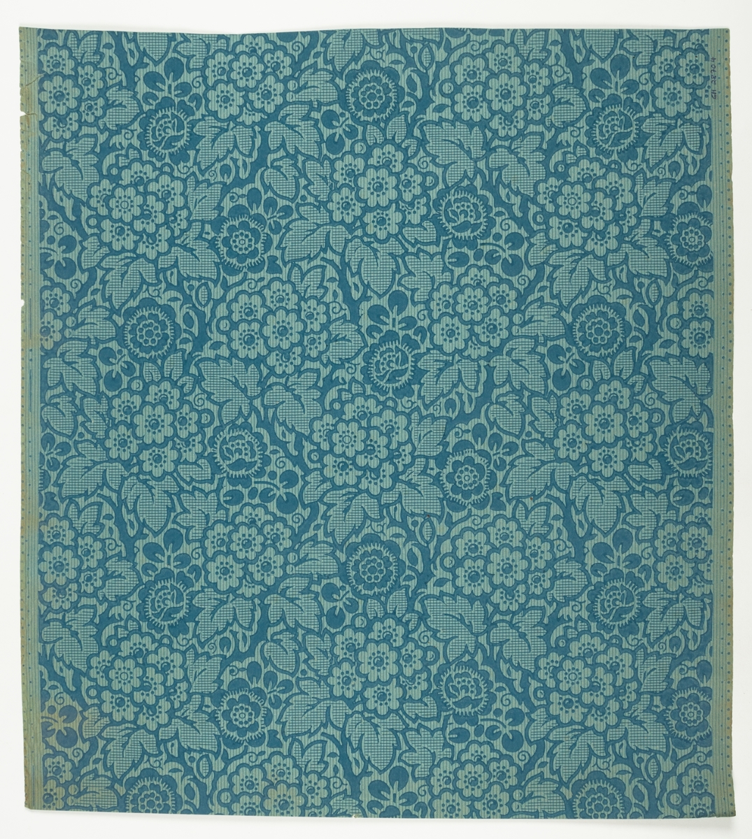 Tapet med tätt, yttäckande mönster av blommande grenar, s.k. gobelängtapet i blått på obestruken botten av blågrönt genomfärgat papper. Underliggande rastertryck. En tryckfärg plus raster. IB