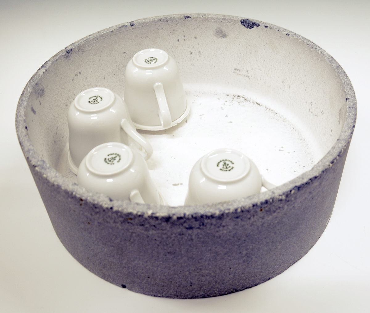 Rund kapsel i ildfast stein med syv porselenskopper på bumser/styringer (Merket A-G).