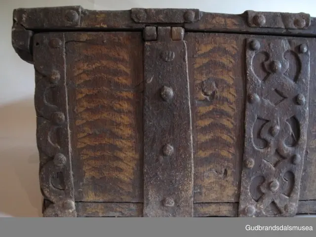 "Rik gjenombroten jarning over heile skrinet. Gamal type, alder uviss. Fra Vestre Gausdal". (Jf. "Katalog for Lom Bygdesamling,1925"). 
Skrinet har 3 rom, nøkkelhullslås og jernhandtak på sidene. Lokket er satt sammen av 2 bord, er festet til utsiden på bakstykket med to hengselbeslag og har 2 sidelister festet med trenagler. Bunnen er satt sammen av 2 bord, festet til hverandre med 2 forsenka trenagler; bunnen er festet til skrinrammen med trenagler.  Skrinrammen er tappet og forsterket med hjørnekantbeslag utvendig. 
Skrinet har jernbeslag med gjennombrutt mønster, 5 stk. B: 6,5 x L: 45 cm på lokk, 3 på hhv. bakstykke, front og sidestykker B: 6,5 x 20 cm. Lokket har ett låsbeslag og de to øvre hengselbeslag festet på innsiden, de to nedre hengselbeslag er festet på utsiden av bakstykket. Alle beslag er festet med store jernnagler samt festet under bunn på skrinet. De to hengselbeslag har også gjennombrutt mønster.  Nøkkelhullslåsen mangler låsanordning på innsiden.
DEKOR. Malingen har blitt beskyttet med et lag ferniss el.l., noe som ble vanlig fra begynnelsen av 1700-tallet. Ingen skurddekor. I stedet er beslag av jern brukt som dekorelement, noe som periodemessig kan peke på 1600-tallet, tidlig 1700-tallet, der treskurden ikke var fremherskende. Liknende dekorbruk finner du på LBY0328. Skrinet har gjennombrutt mønster på beslag og store jernnagler som beslagfeste. Treverket som synes mellom beslagene er malt med horisontale bølgestrukturer i gul og brun. Den dominerende dekorfargen er brun og gul, men det finnes små rester av blå eller blågrønn på lokk, sidelister på lokk, front og bunnkant på bakstykket samt av gul på frontbeslag. Innsiden av lokket er malt i terracottarød nyanse. Tradisjonelt fremkom denne fargen ved bruk av saft fra orr blandet med spytt, som ble smurt ut over treet. 
BRUK. Før kofferten kom i bruk hadde man reiseskrinet, som ble brukt til oppbevaring av bl.a. klær, verdisaker og mat på reiser. Skrinet hadde ofte et eller to mindre, smale rom langs den ene skrinsiden og ett større rom. De fleste reiseskrin var i tillegg forsterket med jernbeslag langs alle kanter og med en solid nøkkelhullås til sikring mot støt, slag og tyveri.