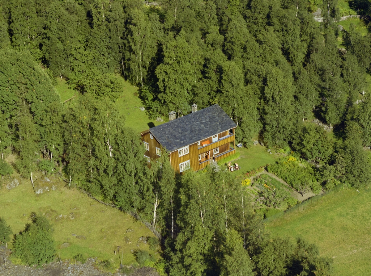 Gårdsbruk Alme, malingsslitt rød driftsbygning, hvitt våningshus og to brune uthus med dyrket mark rundt.