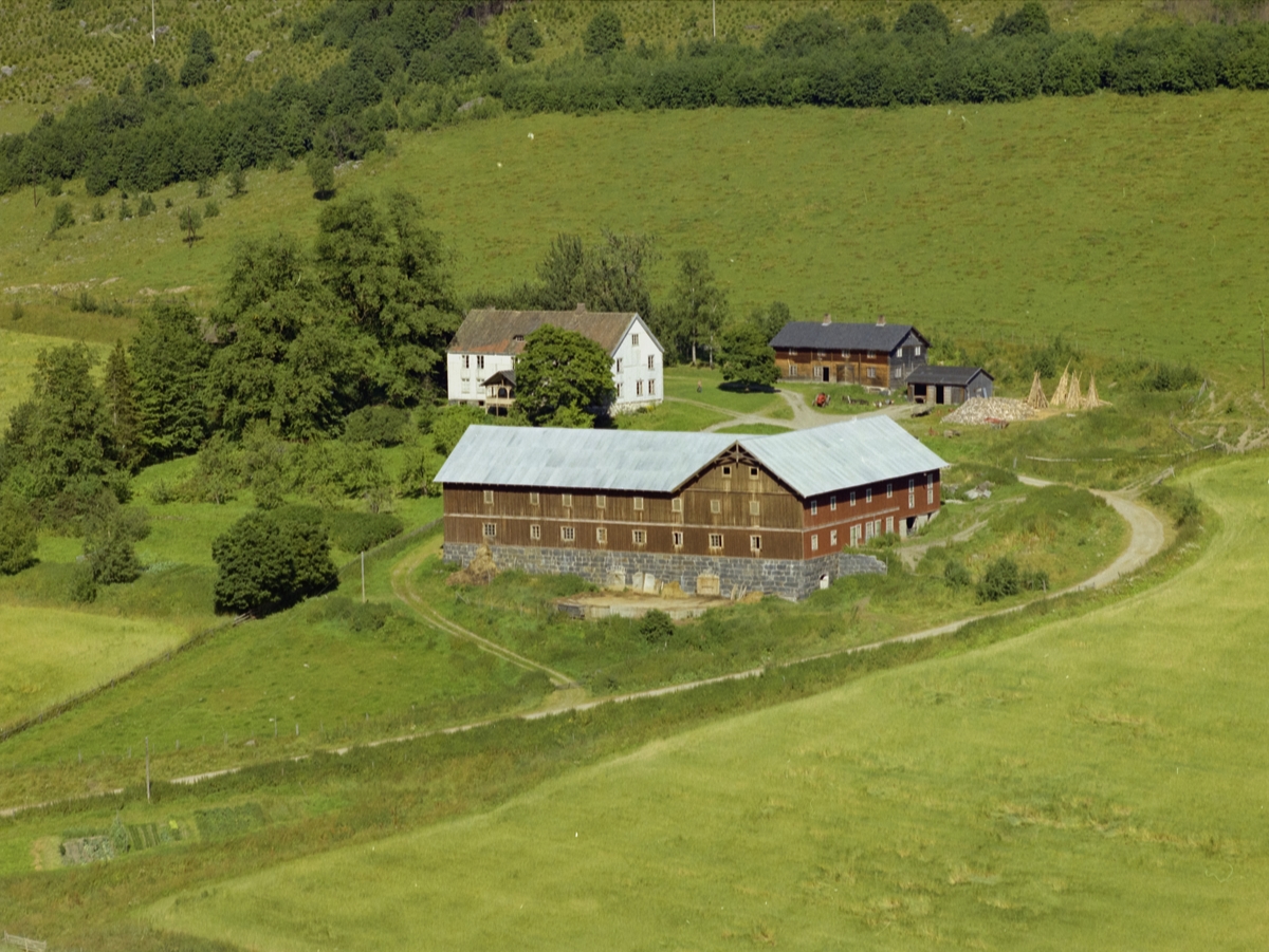 Rokvam. Gårdsbruk. Hvit bygning med hage, liten brun bygning, vinkelbygd stor driftsbygning. Åkrer og utmark.