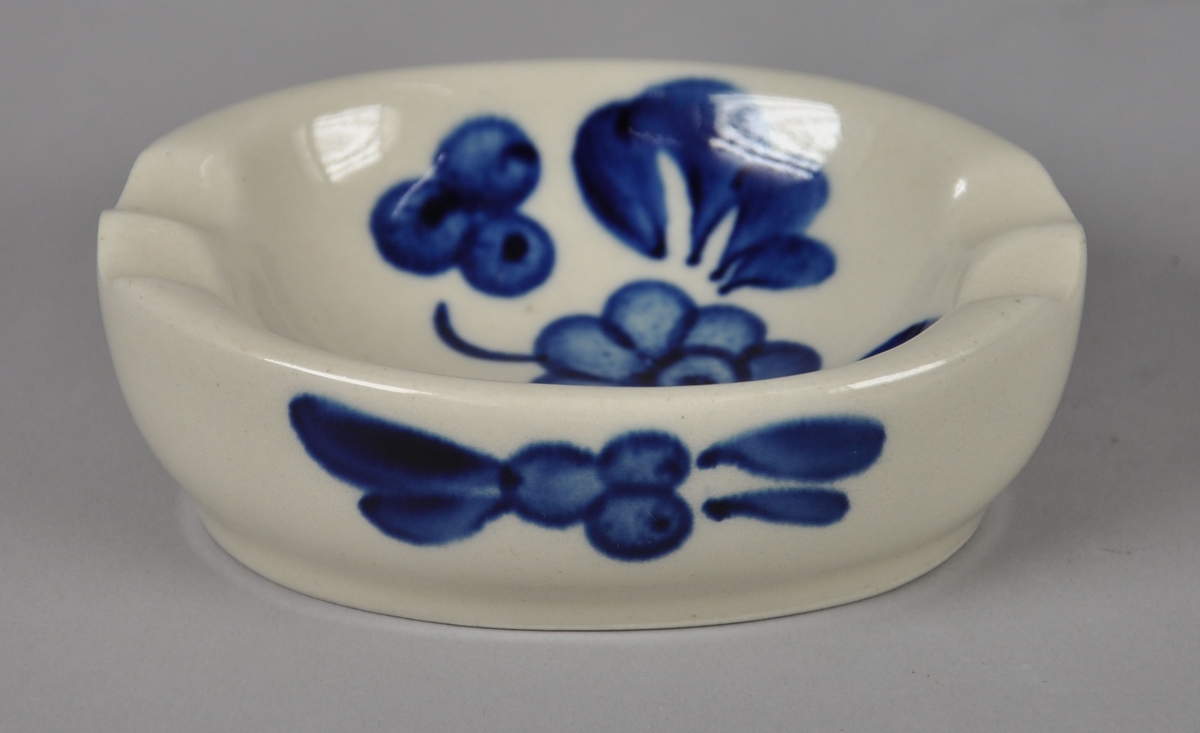 Oval sopeholder av glassert keramikk. Har malt dekor med motiv av blå blomster, blader og bær.
