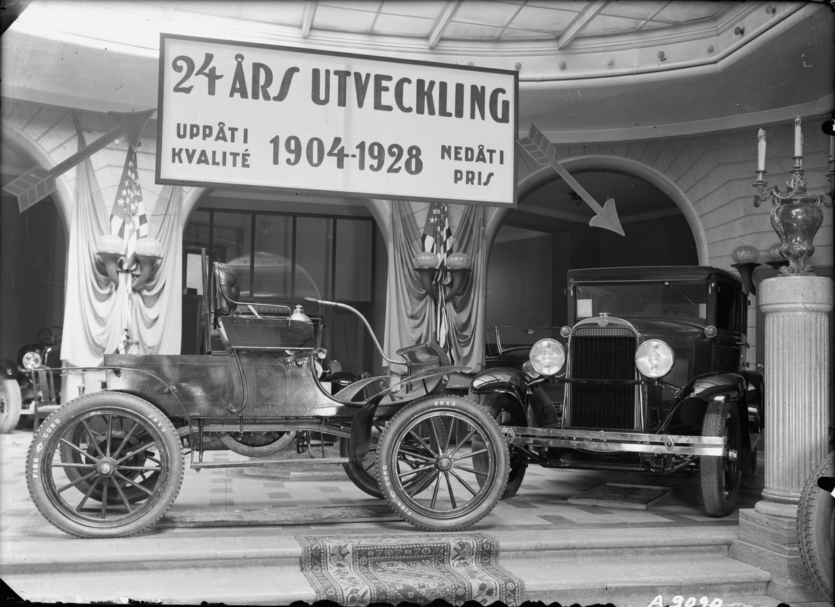 Bilar på utställning i Ostermans marmorhallar. Skylt: "24 års utveckling. Uppåt i kvalité 1904-1928 nedåt i pris.". Bland annnat Oldsmobile Curved Dash.