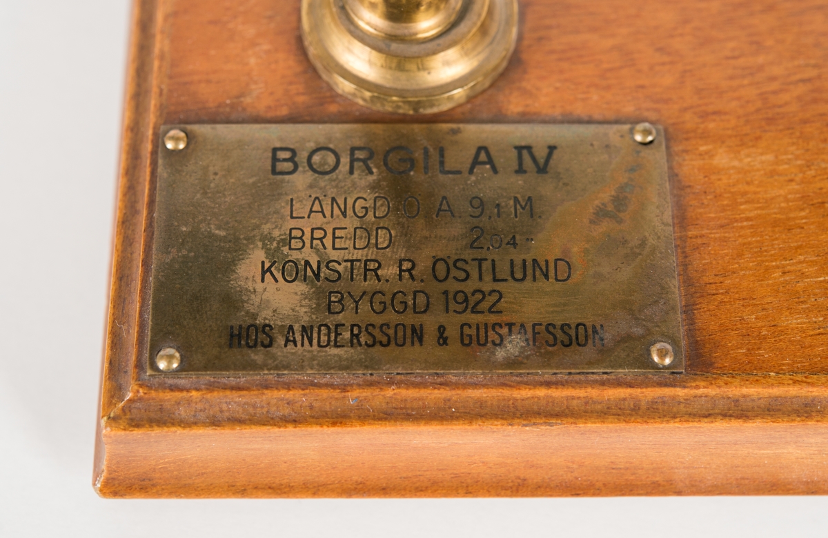 Modell av Borgila IV  som i original konstruerades av R. Östlund och var 9,1 m lång och 2,04 m bred.
Modellen har standert i masttoppen och flagga i fören, liksom ankare på fördäck.