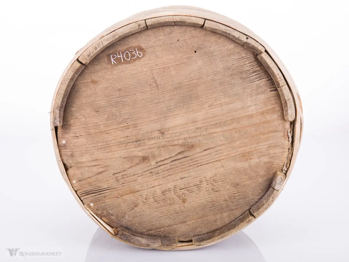 Rund med 3 vidjeband nede og 2 oppe og ører til lokk som mangler. Utskjæringer i relieff på hver stav.