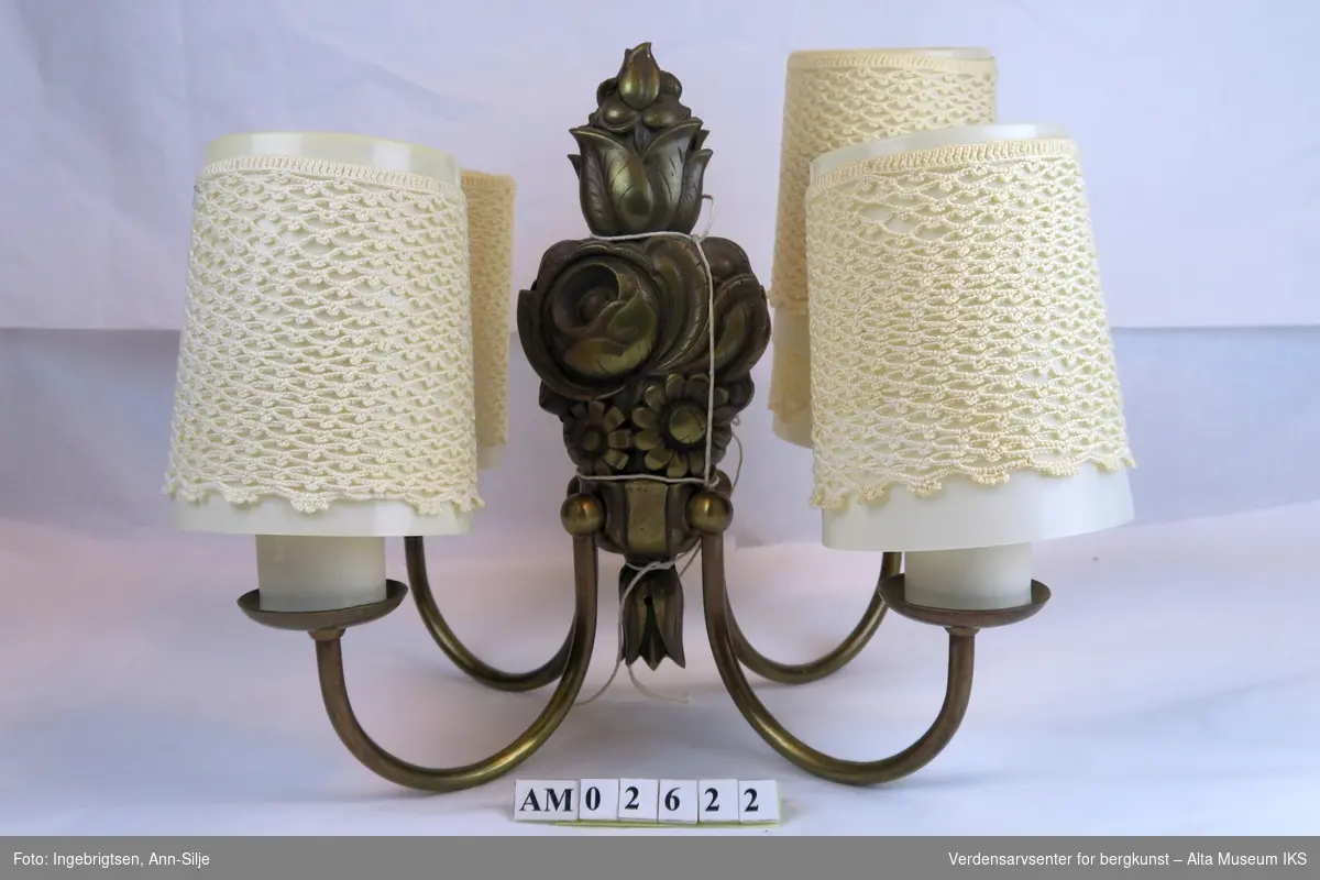 Form: 2 to-armede lampetter, plastskjermer med heklet overtrekk. Det er blomstermotiv på veggfestet.