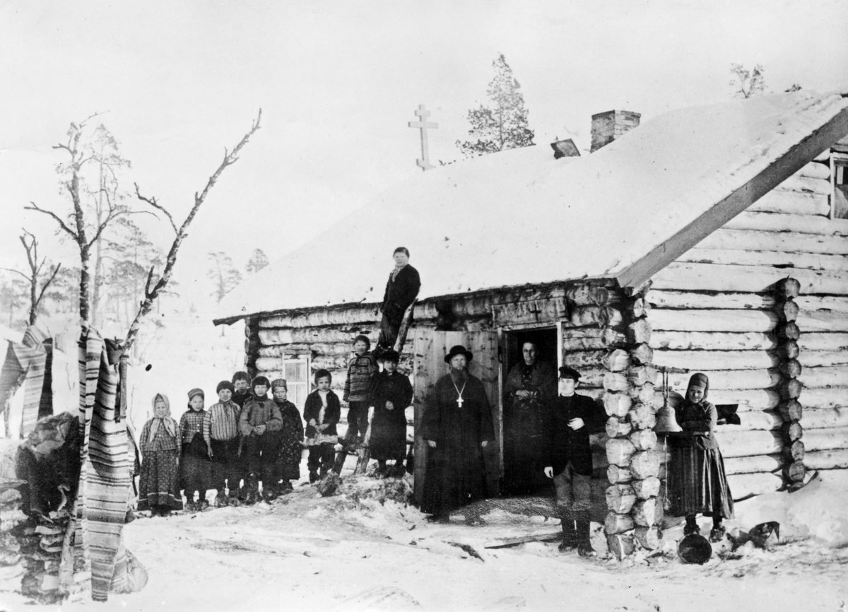 Prosten med kone, klokkeren og skoltesamiske skolebarn ved russisk skole og kapell, Pasvik, Sør-Varanger, Finnmark,  ca. 1898. 