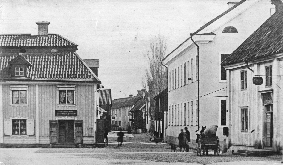 SV hörnet av Torget före branden med Roséns gård och grosshandlare Erikssons gård. Huset rakt fram med karolinertak, gård 116, tillhörde Erik Bellinder, som där bedrev diversehandel.
