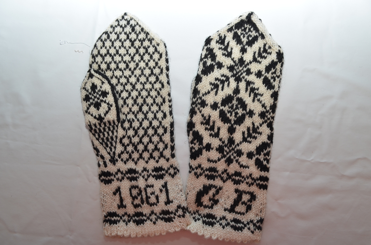 Vott (a+b), rosestrikket i svart og hvitt ullgarn. Bokstavene GB og årstallet 1961 er strikket inn i begge linningene.