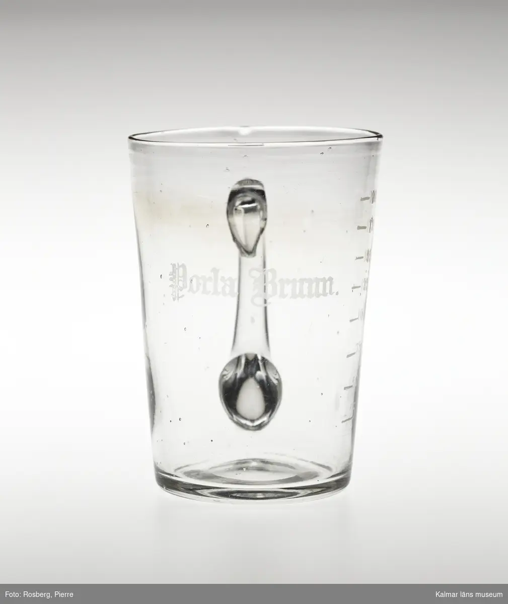 KLM 28155:1 Hankglas, av glas. Glaset är avsmalnande neråt med lodrät grepe. Slipad text, Porla Brunn och måttsticka för, 25, 50, 75, 100, 125, 150, 175, 200.