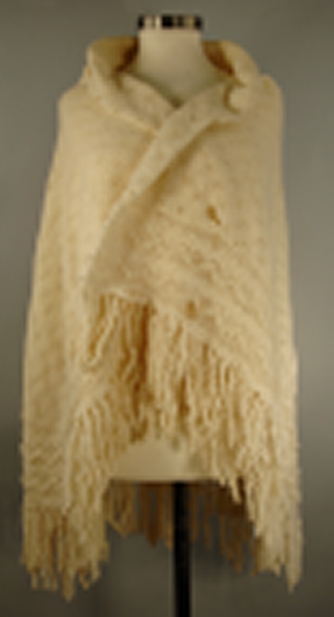 Strikket i tynn ulltråd. Den innerste firkanten er strikket i eit stykke. Knaten rundt påsydd slik at hjørnsne blir avrunda. Dersetter er det påsydd frynser med symaskin.