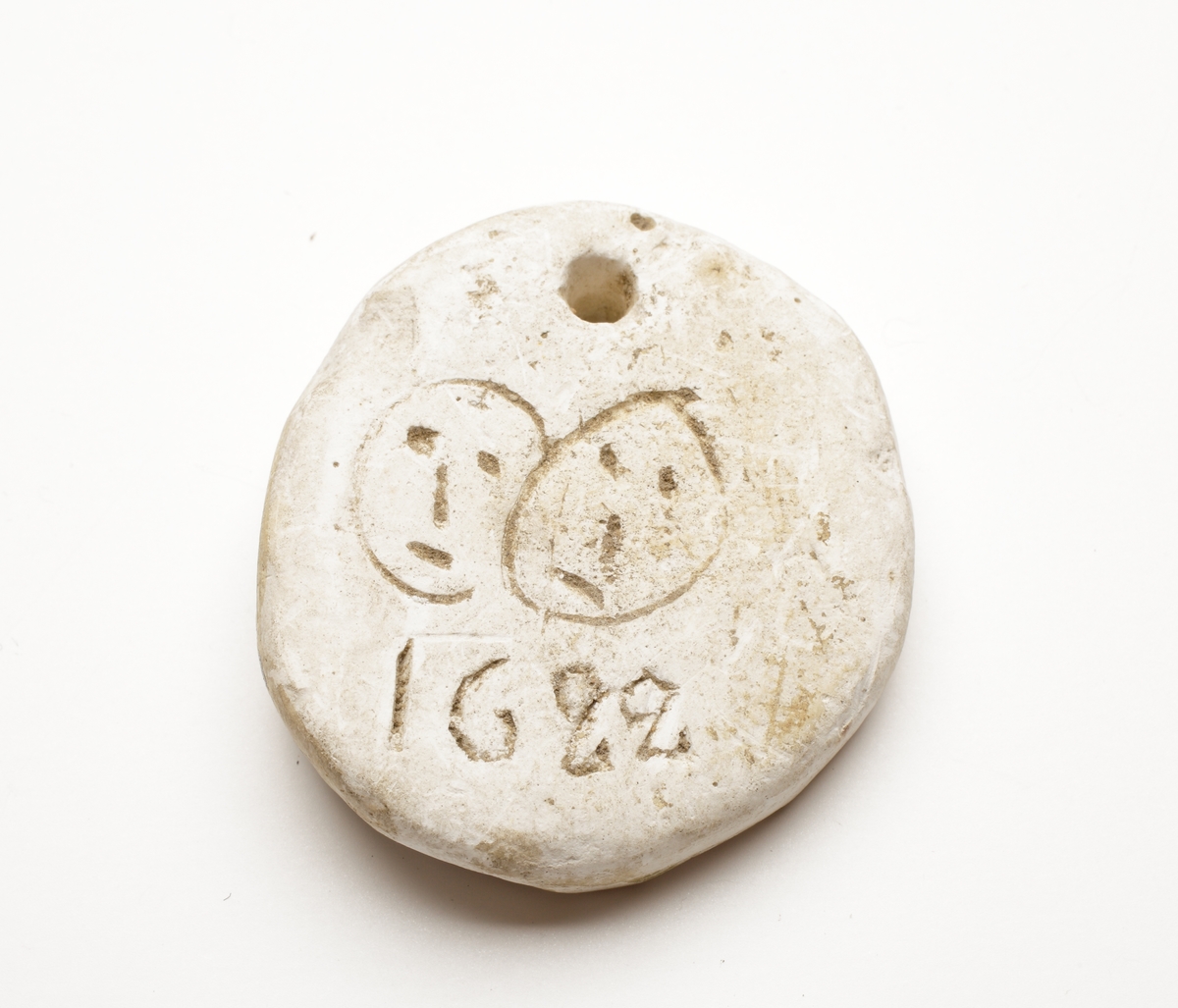 Rund medaljong av gips med två inristade ansikten (streckgubbe) och talet 1622.