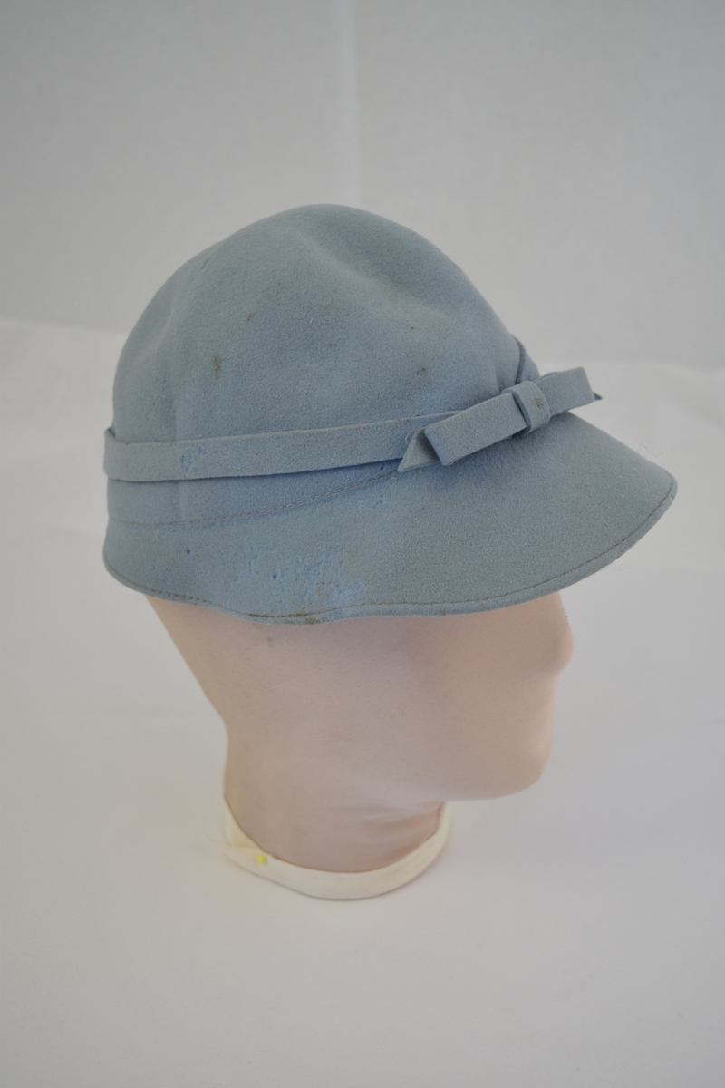 Rund hatt med brem som smalner på hattens bakside. Påsydd bånd med sløyfe. Form: bolleform