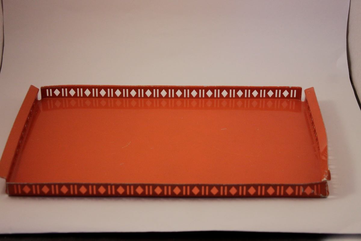 Rektangulär orange plåtbricka. Kant med hålmönster två streck och en romb som upprepas runt brickans kant. på kortsidorna är kanterna böjda som handtag.