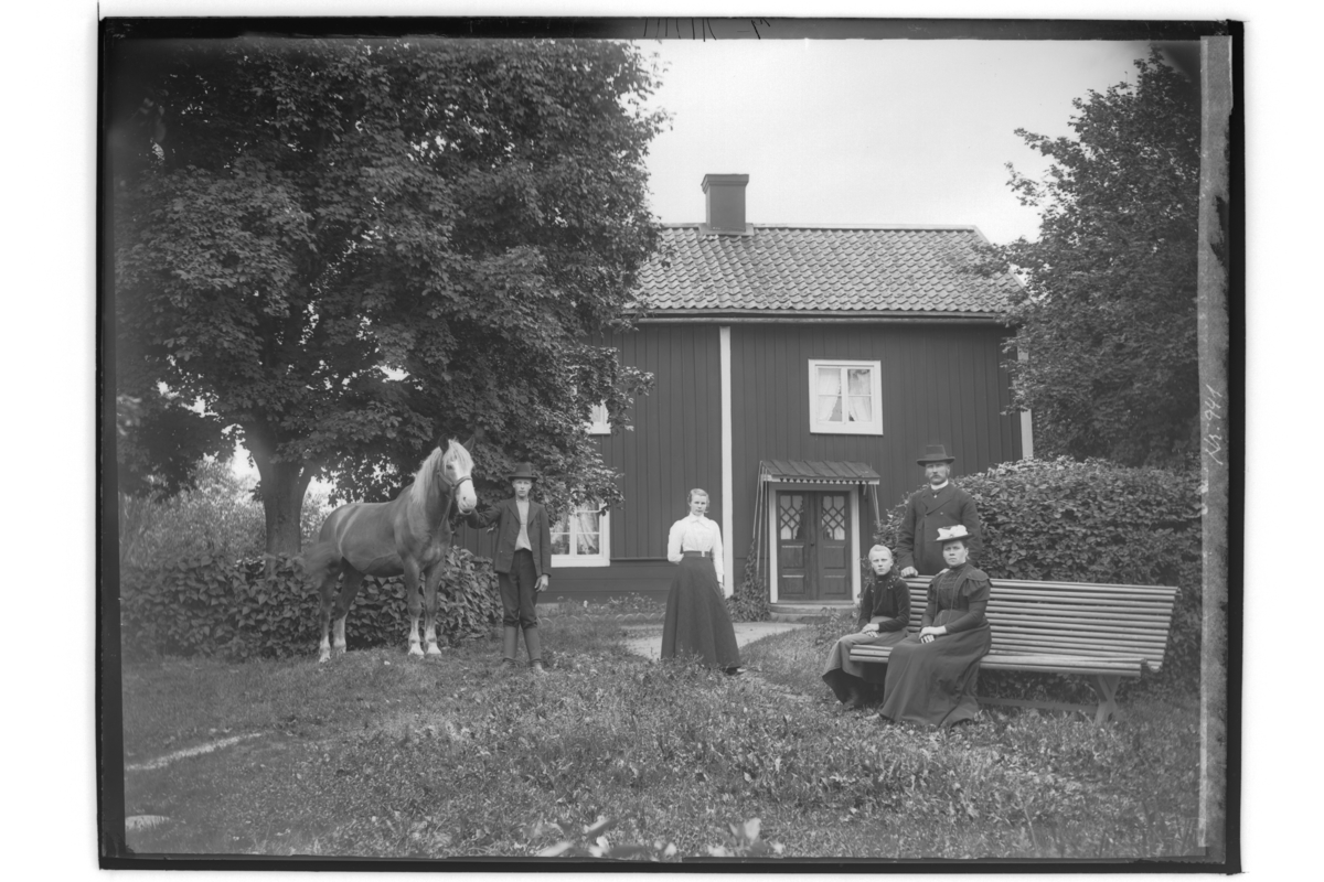 Tvåvånings bostadshus, närkesstuga. 
Familjegrupp 5 personer och en häst framför stugan.
C.O. Erikson.