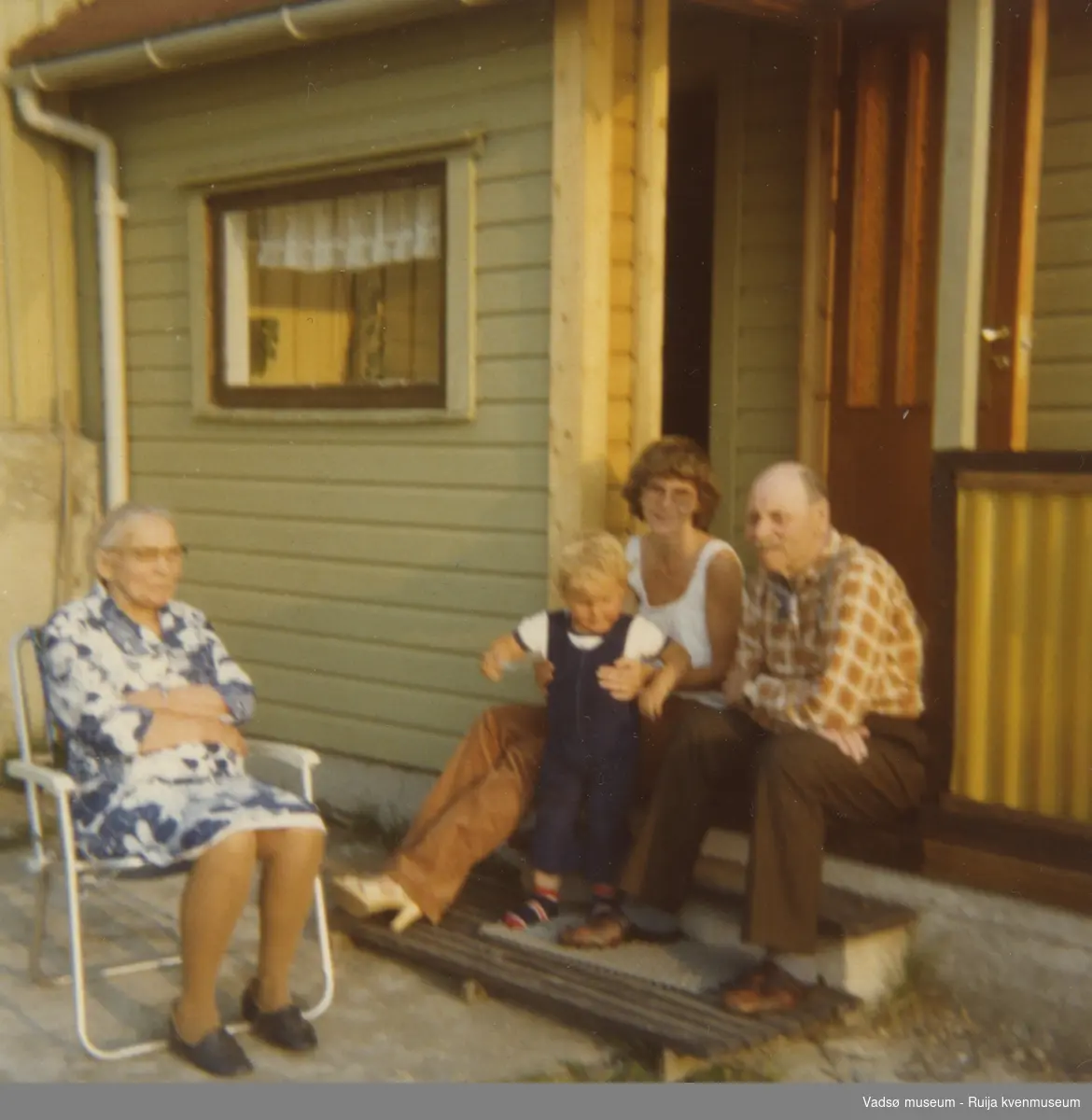 Daniel og Anna Jørstad med barne- og oldebarn sittende på trappa utenfor huset på Hellestvedt, Ekkerøy, ca. 1971/72.
