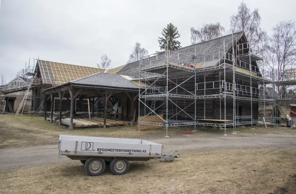 Foto som viser Tomterlåven med stillas rundt og delvis ny lekting på taket. personbilhenger i forgrunnen.