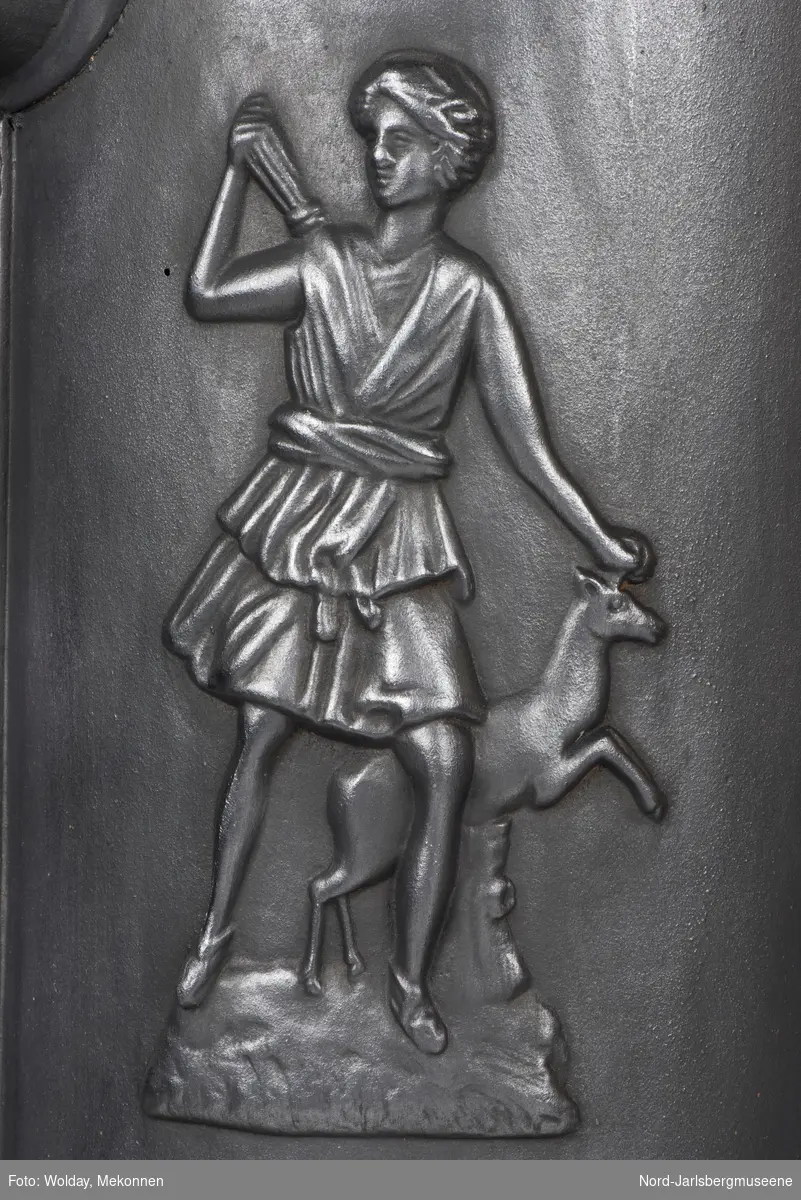 Jugendstil. Askeskuff med et slags bålmotiv, fyrdør med rosett. Relieff av klassisk motiv; Diana med hjort?
