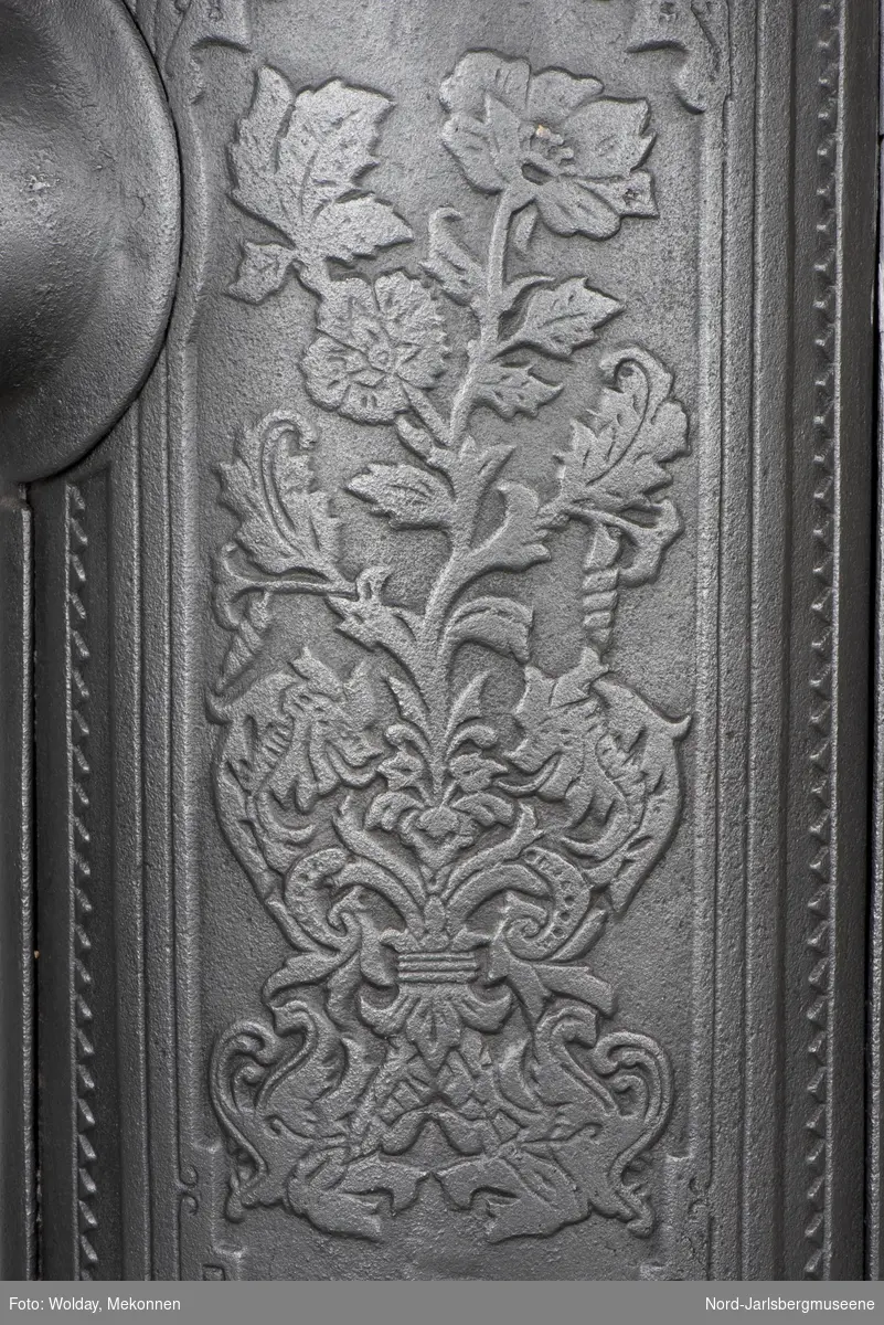 Ovn i jugendstil, stilisert planteornamentikk ("roser") på dører, ellers vikingtidsinspirert dekor med dragemønster på topplokk.  De to sideplatene er dekorert med blomsterornament, innrammet av en bord i  stilisert jugendmønster (Mac Intosh-inspirert).Toppknott formet som stilisert planteknopp.