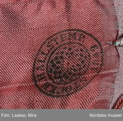 Huvudliggaren:
"a-r Kvinnodräkt. a. kjol, b. förkläde, c. kappa, d. tröja, e. överdel
f.1 - f.4 huvudbonad, (4 delar), g. bälte, h. kjolsäck, i. handskar, j: silkesduk, k. bokkläde, l. psalmbok, m.1- m.2 Bältehängen med silversked och skedpåse, n. nåletui, o.1 kniv, o.2 gaffel, o.3 slida av saffian, p. lit. påse, q. kedjekniv, r. ring.  Ink. 13/7 1903 [från] Eriksson, Erik, herr, Kåsta, Vingåker jämte 95.162 [...]. [Brukningsort:] Södermanland Oppunda hd Vingåker sn."

b. Högtidsförkläde längd 96 cm, vådbredd 80 cm. Av grön rask, nedtill kant och skoning av svart kläde, upptill 3 cm bred linning av svart kläde. Nederkanten broderad med en vågrad i kedjesöm med gult silke, ovanför denna en staket-och 6 stjälksömsrader i omväxlande gult och rosa silke samt e rader band av ylle och silke i lila, rött o gult. Linningen broderad med tre rader flätsöm i lila och gult. På sidor om linningen 6 cm fria ändar. Knytband av mönstrat bomullsband.

d. Tröja, s.k. bindtröja , mycket kort, slutar under ärmarna. Av svart fint kläde med  stora spännen på röda klädesmattor. Foder av blekt bomullslärft, ståndkrage ca 3 cm hög, hansdledslinningar ca 3 cm breda med röda passepoaler, ärmsprund knäppt med hake och hyska.

e. Överdel till kvinnodräkt, kort modell som når nedanför brösten,  av vit tunn bomullslärft, ett bålstycke fodrat med vit bomullskypert, öppen fram, rak nedvikt krage med en liten broderad bård i vittbomullsgarn, Både krage och framkanter kantade med en  2,5 cm bred maskinknypplad uddspets.
/Berit Eldvik 2010-08-27

f: 1-4 Huvudbonad "Huckel"
f:1 Sydd cylinderformad stomme av halmflätor med stödande träpinne i kullen. Höjd omkr. 23 cm
f:2 Fyrkantigt tygstycke av bomullslärft, svept kring stommen.
f:3 Mössa av rött kläde broderat med gult, brunt och grönt silke i tambursöm.
f:4 Kvadratiskt kläde av vit bomullslärft, vikt i tresnibb, stärkt och goffrerat. Snibben nedvikt över den röda mössan, dock utan att helt och hållet skyla densamma.

g. Bälte, längd 69 cm utan spänne, bredd 7,5 cm.
Av styvt skinn överklätt med rött ylletyg och besatt med 14 kupiga silverbucklor med punsad dekor, kraftigt spänne av samma typ med hake och ögla. På spännet flera stämplar bl.a 3 kronor, I P samt C.
/Berit Eldvik 2007-02-20