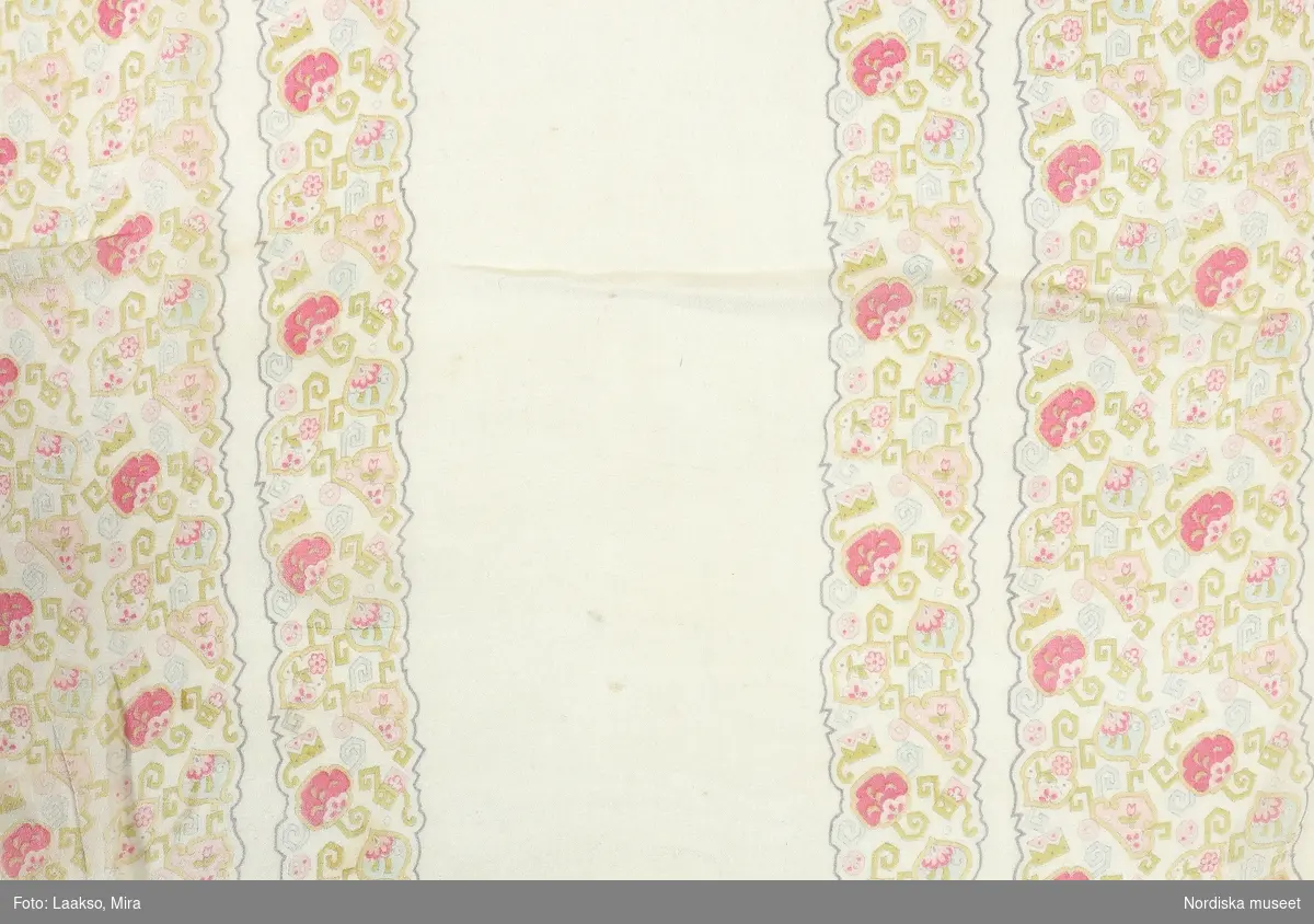 Lång schal av tunn silkecrépe, vit med bårder längs båda långsidorna med tryckt mönster med orientaliskt påverkat blommönster i kantig stil i pastellfärger av rosa, ljusgrönt, gult och ljusblått. Hansydda smala fållar i kortsidorna.
Har tillhört småskollärarinnan Emma Göransson från Kabbarp född 1879. Se även en samling klänningar mm. som visar hennes intresse för kläder och mode.
/Berit Eldvik 2012-01-13