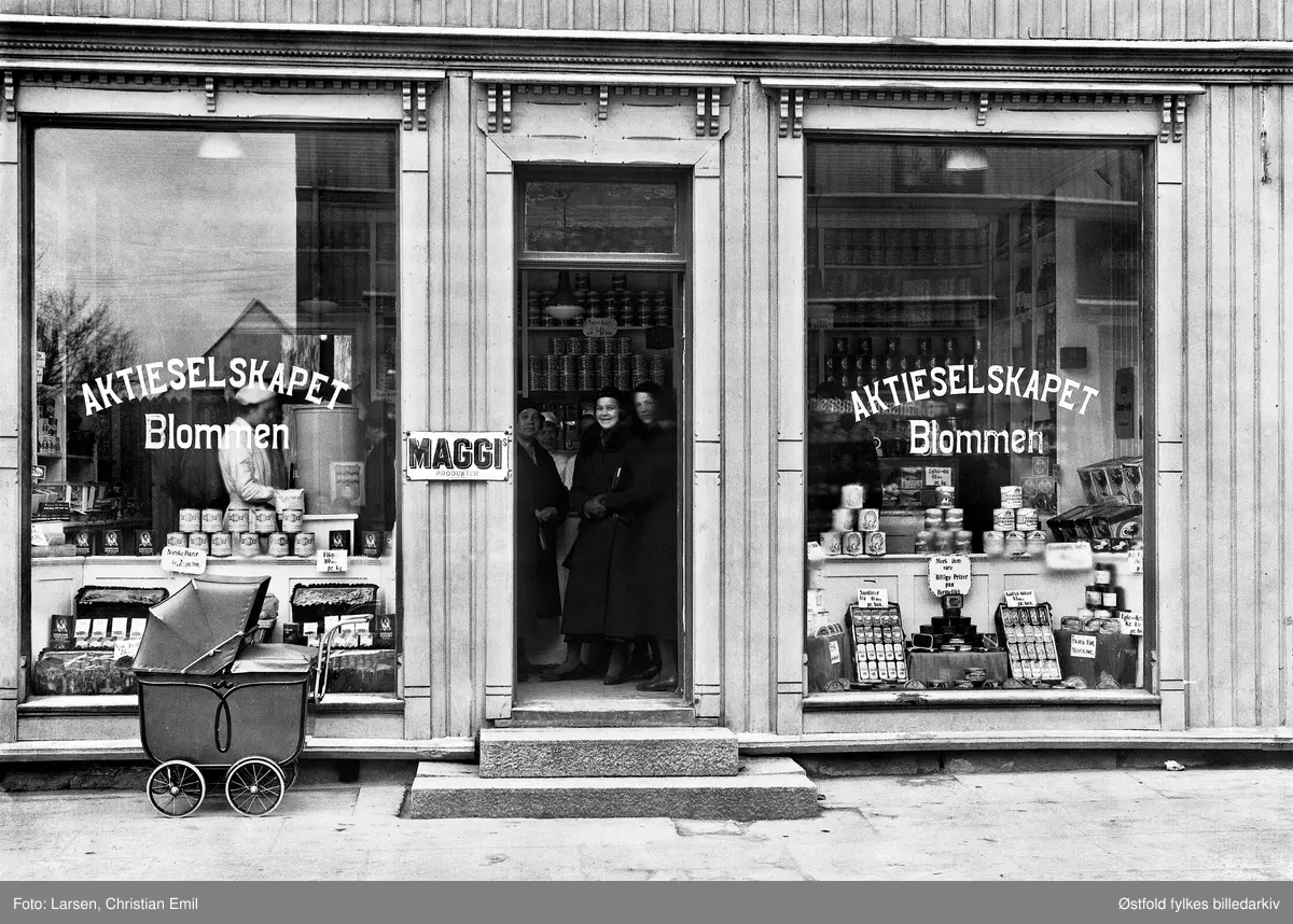 Forretning Aktieselskapet Blommen, i St. Mariegate 66 i Sarpsborg,  1933. Reklameskilt med MAGGI. Butikk med salg av matvarer. 

Butikken  ble etablert i 1933. Butterly Konditori flyttet inn i lokalene i 1937.

Det reklameres blant anna for "Faarikaal, Taffel-Ost, Fikner, Gaffel-Bitter, Sardiner, Norske pærer, Sjokoladepudding, Ekstra fint meierismør, De fortrinlige MAGGIs produkter". Og til sist: "Merk dem Vore billige priser paa hermetikk".