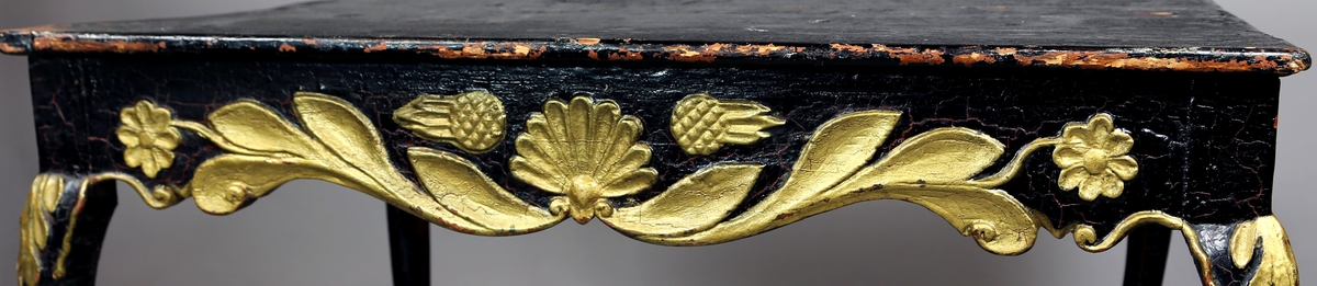 Svart bord med buede bein og utskjæringer malt i gull langs kantene av underramme og øvre del av bein.