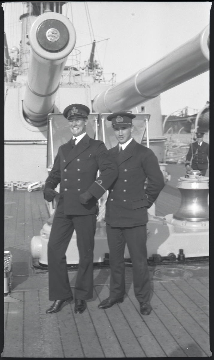 Två sjöofficerare med fänriks grad poserar på däck under tungt artilleri på pansarskepp, till h Gunvald Berger.
