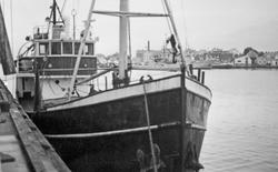 Fiskebåt ved kai. Bybebyggelse i bakgrunnen.
