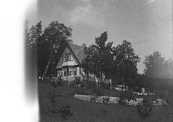 Sommer. Hus omkranset av en veranda.  Flere personer sees på