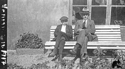 Sommer. En gutt og en mann sitter i solskinnet på en benk ut